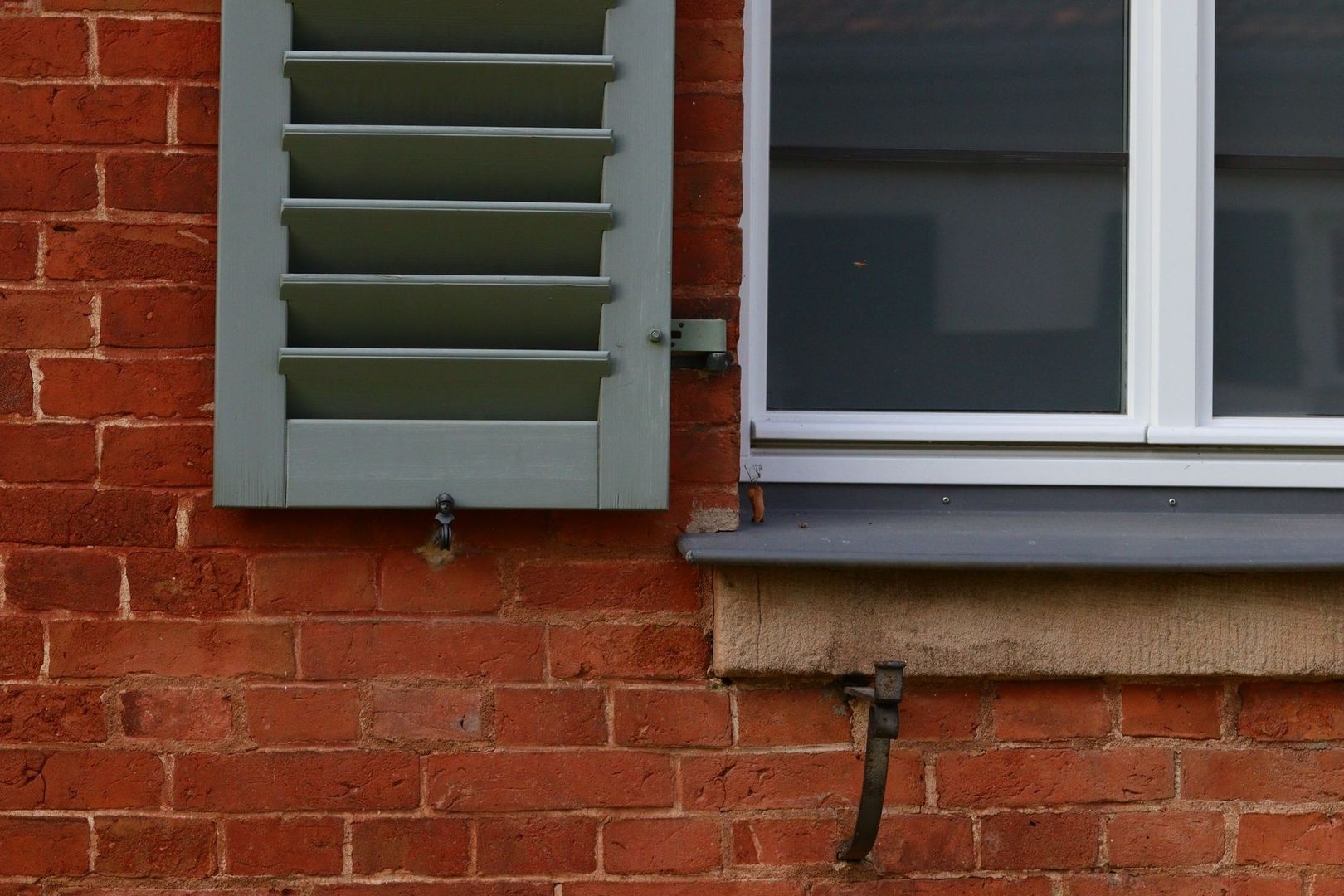 Detail eines historischen Ziegelfensters mit grauem Holzladen und Kastenfenster